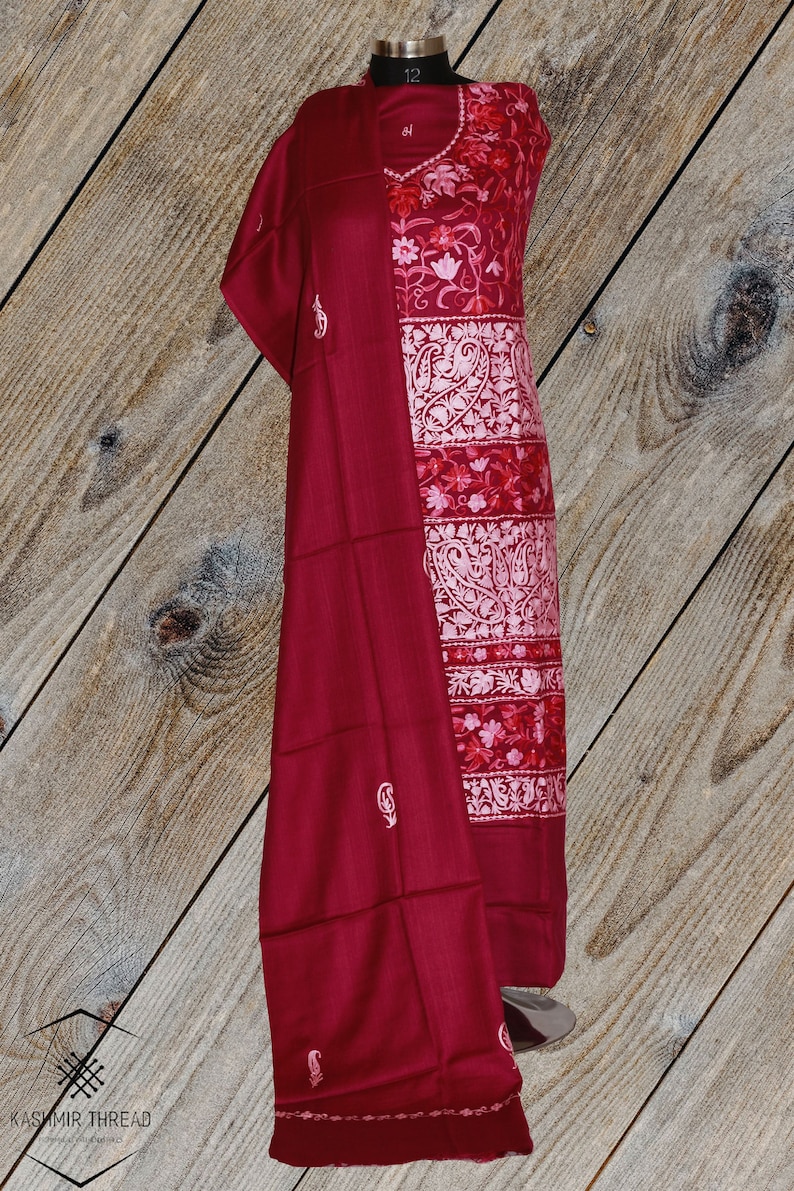 May include: A maroon shawl with white embroidery and a matching maroon dress with white and pink floral embroidery. The dress and shawl are displayed on a mannequin against a woodgrain background.