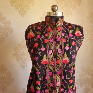 May include: A black sleeveless vest with a mandarin collar and floral embroidery in shades of pink, red, and green.