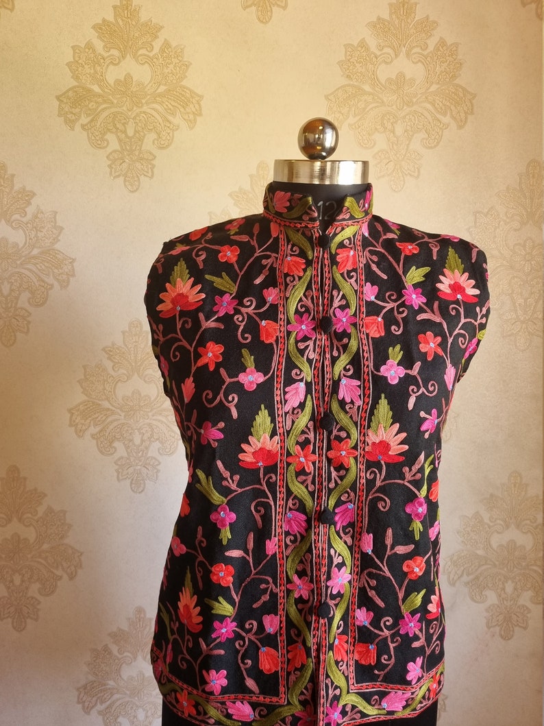 May include: A black sleeveless vest with a mandarin collar and floral embroidery in shades of pink, red, and green.