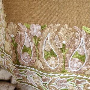 K&ouml;nnte beinhalten: Ein brauner Schal mit einem detaillierten bestickten Rand mit floralen und Paisley-Motiven in Gr&uuml;n-, Wei&szlig;- und Beiget&ouml;nen.