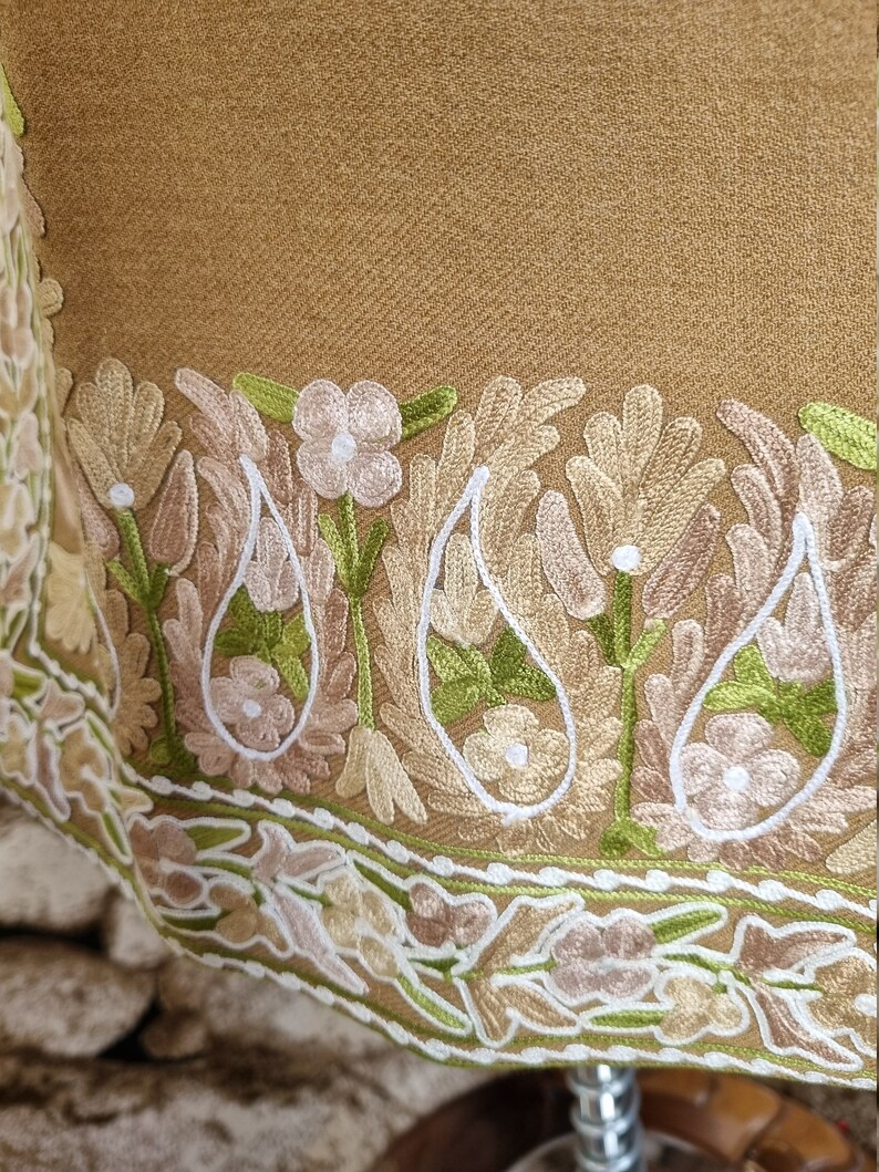 K&ouml;nnte beinhalten: Ein brauner Schal mit einem detaillierten bestickten Rand mit floralen und Paisley-Motiven in Gr&uuml;n-, Wei&szlig;- und Beiget&ouml;nen.