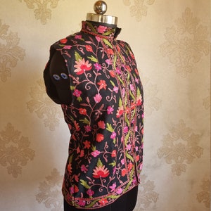 May include: A black sleeveless vest with a high collar and floral embroidery in shades of pink, red, and green.