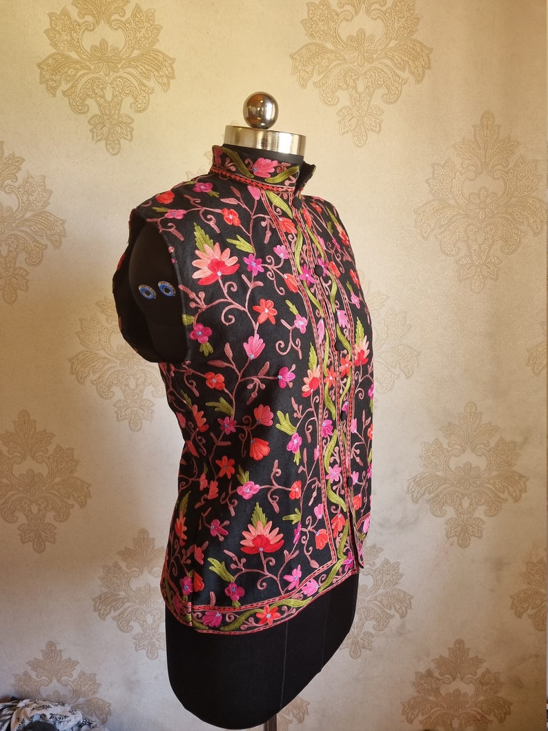 May include: A black sleeveless vest with a high collar and floral embroidery in shades of pink, red, and green.