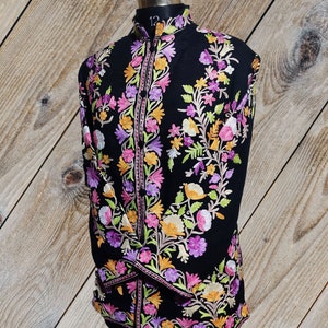 May include: A black long-sleeved shirt with a mandarin collar and intricate floral embroidery in shades of pink, purple, yellow, and green.