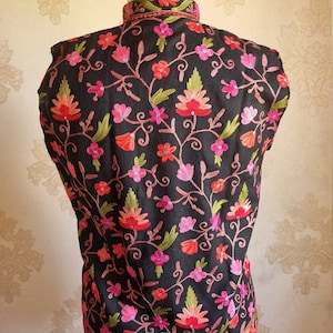 May include: A black sleeveless vest with a high neck and intricate floral embroidery in shades of pink, red, and green.