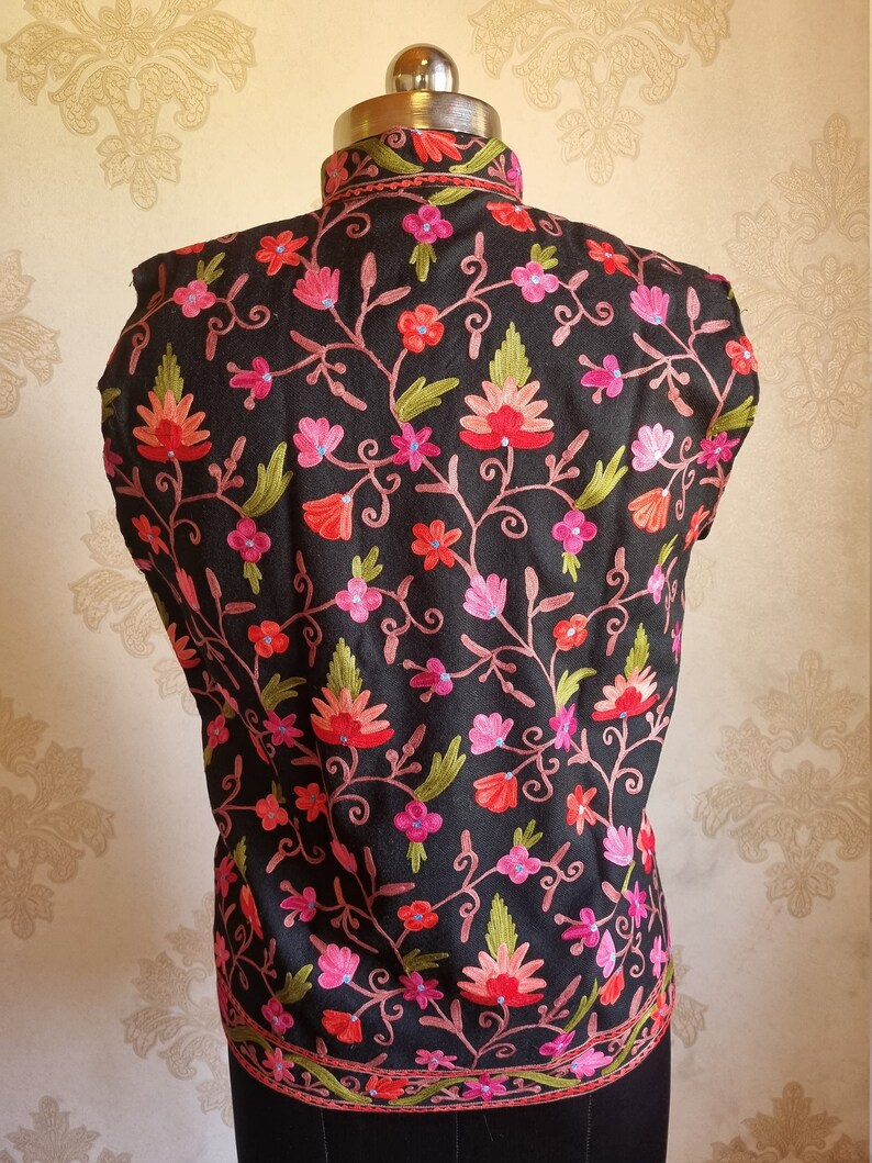 May include: A black sleeveless vest with a high neck and intricate floral embroidery in shades of pink, red, and green.