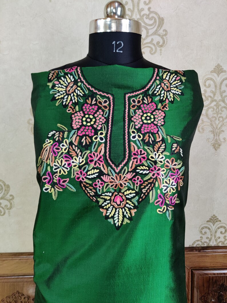 May include: A green silk kurta with a floral embroidery design. The embroidery is in shades of pink, white, and yellow.