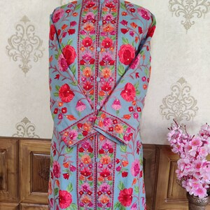May include: A long, light blue embroidered coat with a mandarin collar and floral patterns in shades of pink, red, and green.