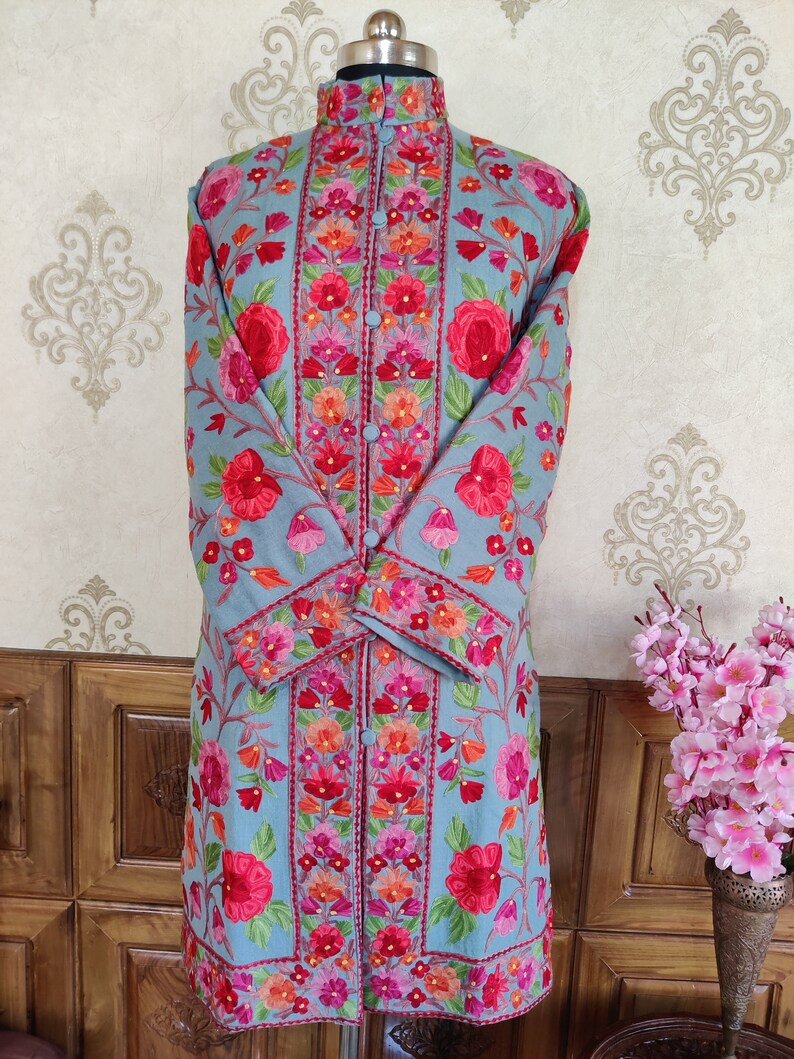 May include: A long, light blue embroidered coat with a mandarin collar and floral patterns in shades of pink, red, and green.
