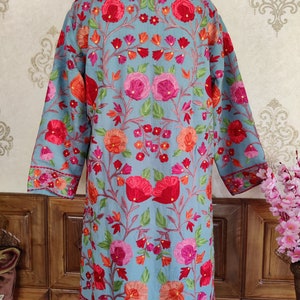 May include: A long, light blue embroidered jacket with a floral pattern in shades of pink, red, and orange. The jacket has a mandarin collar and long sleeves.
