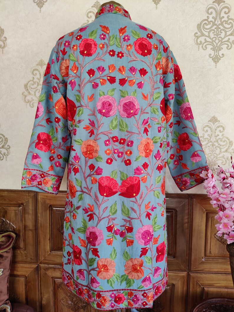 May include: A long, light blue embroidered jacket with a floral pattern in shades of pink, red, and orange. The jacket has a mandarin collar and long sleeves.
