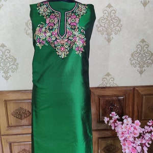 May include: A green sleeveless tunic with a floral embroidery design on the neckline. The embroidery is in shades of pink, white, and green.