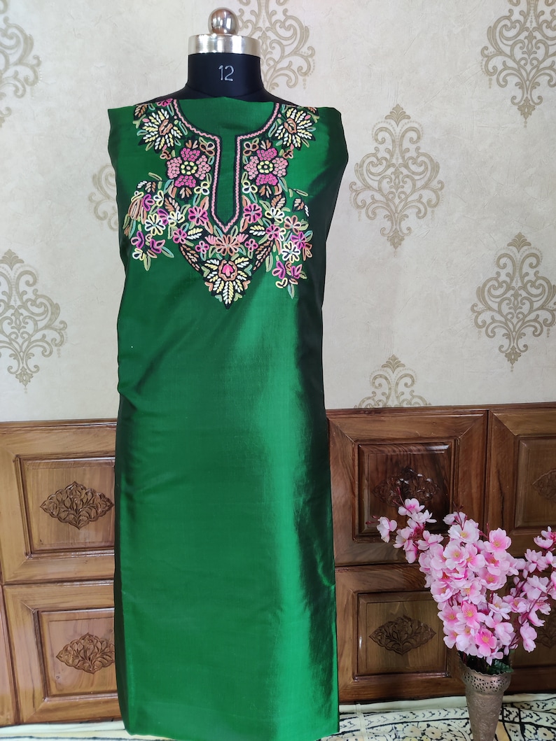 May include: A green sleeveless tunic with a floral embroidery design on the neckline. The embroidery is in shades of pink, white, and green.