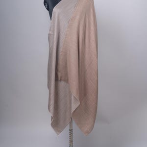 Könnte beinhalten: Ein großer, rechteckiger Schal, der über eine Schaufensterpuppe drapiert ist. Der Stoff hat ein zweifarbiges Design mit einer Seite in hellem Beige und der anderen in einem warmen Hellbraun. Das Material weist eine feine Webstruktur auf.