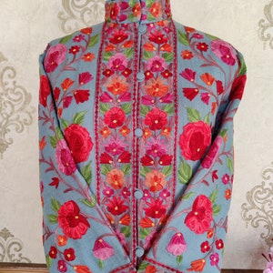 May include: A long-sleeved, light blue embroidered jacket with a mandarin collar and floral embroidery in shades of red, pink, orange, and green.