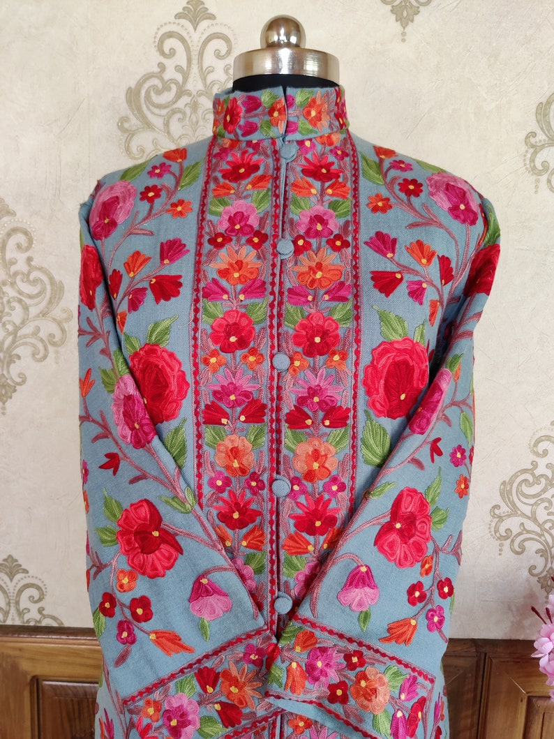 May include: A long-sleeved, light blue embroidered jacket with a mandarin collar and floral embroidery in shades of red, pink, orange, and green.