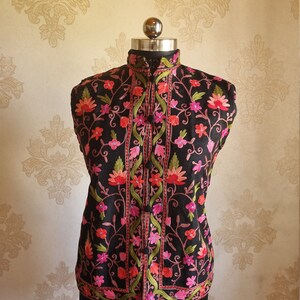 May include: A black sleeveless vest with a high collar and floral embroidery in shades of pink, red, and green.