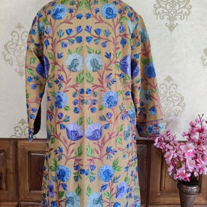 May include: A long, beige embroidered jacket with a floral pattern in shades of blue, green, and pink. The jacket has a mandarin collar and long sleeves.