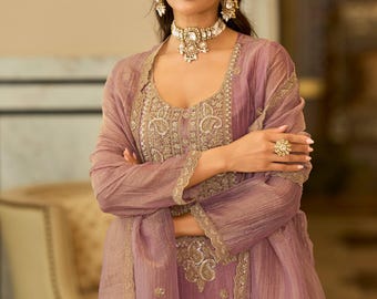 May include: A mauve-coloured ensemble featuring a sleeveless bodice and a matching sheer long-sleeved overlay, both adorned with intricate gold embroidery. The outfit includes a coordinating choker necklace, dangling earrings, and a maang tikka.