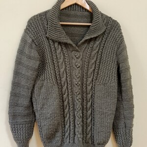May include: A dark green knitted sweater with a cable knit pattern and a collared neckline.
