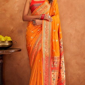May include: A woman wearing a yellow and red saree with intricate gold embroidery. The saree has a floral and paisley design. The woman is wearing a red blouse and gold jewelry.