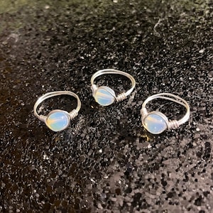 May include: Three silver rings with opal stones. The rings are simple and delicate, with a single opal stone set in each ring.