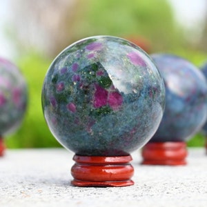 May include: Four green, blue, and pink gemstone spheres on wooden stands. The spheres are polished and have a reflective surface.