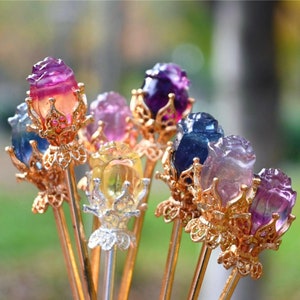 May include: A bouquet of seven gold-toned rose-shaped hair sticks with colourful gemstone tops. The gemstones are in shades of purple, pink, blue, and yellow.
