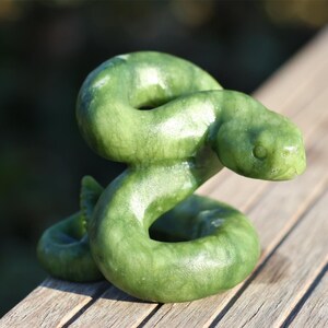 May include: A green jade snake sculpture, coiled and with its head raised, is displayed on a wooden surface.
