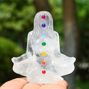 May include: A clear quartz crystal sculpture of a person sitting in a meditation pose with seven colored gemstones representing the seven chakras.