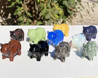 May include: A collection of ten small pig figurines carved from different types of stone. The pigs are in various colors, including green, blue, black, white, brown, and gray.