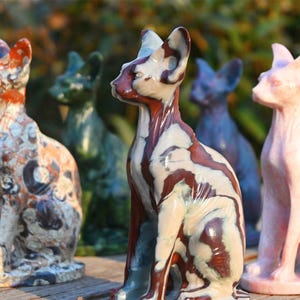 May include: Five ceramic cat figurines in various colors and patterns. The cats are sitting in a row on a wooden surface. The cats are all hairless and have large ears.