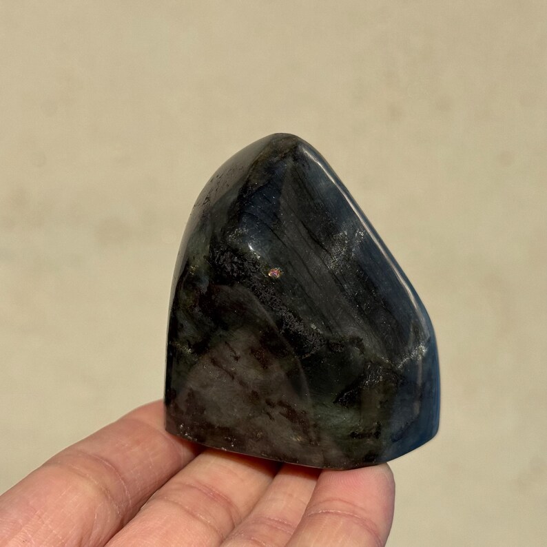 May include: A black and green polished gemstone with a smooth, rounded shape. The gemstone has a unique, striated pattern.