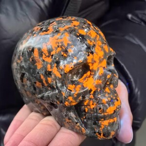 May include: A black and orange skull made of polished stone. The skull has a detailed design and is a unique decorative piece.
