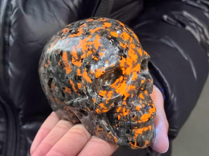 May include: A black and orange skull made of polished stone. The skull has a detailed design and is a unique decorative piece.
