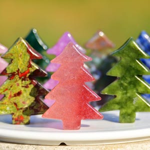 Puede incluir: Colección de figuras de árboles de Navidad de piedras preciosas de colores, incluyendo rosa, verde, rojo y azul, dispuestas sobre un plato blanco. El fondo es borroso, verde y amarillo.