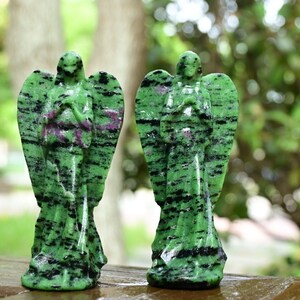 May include: Two green and black gemstone angel figurines with wings. The figurines are carved from a green stone with black and pink streaks.