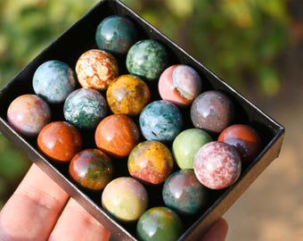 Puede incluir: Una colección de 20 esferas de ágata pulidas y coloridas en una caja negra. Las esferas son de varios tonos de verde, marrón, rojo, amarillo y blanco.