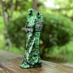 May include: Green and black gemstone angel figurine with wings. The angel is carved from a green stone with black and pink streaks.