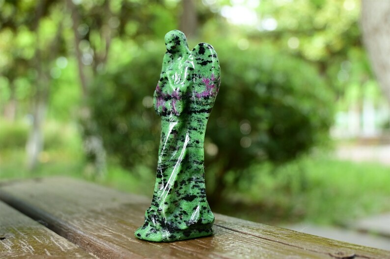May include: Green and black gemstone angel figurine with wings. The angel is carved from a green stone with black and pink streaks.