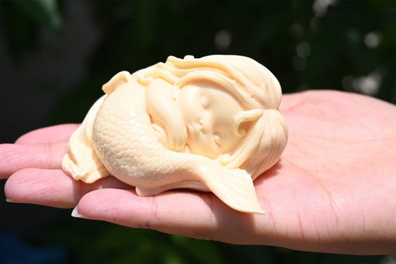 May include: A small, cream-colored figurine of a sleeping mermaid with a detailed tail and long hair.