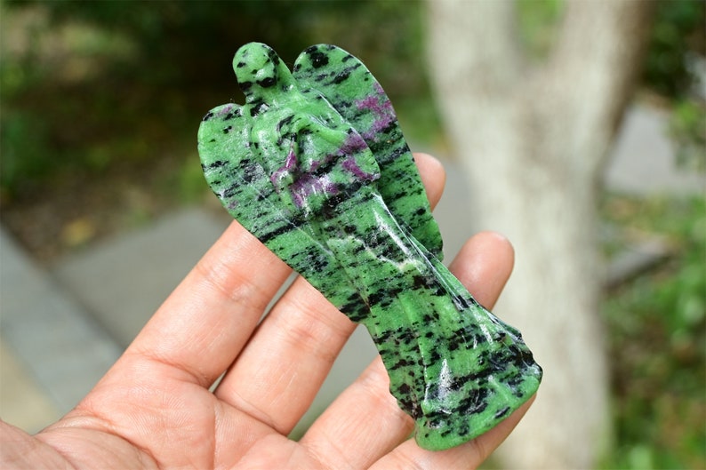 May include: Green and black gemstone angel figurine carved from natural stone. The angel has a detailed design and is a beautiful piece of art.