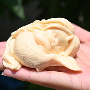 May include: A small, cream-colored sculpture of a sleeping mermaid with a detailed tail and flowing hair.
