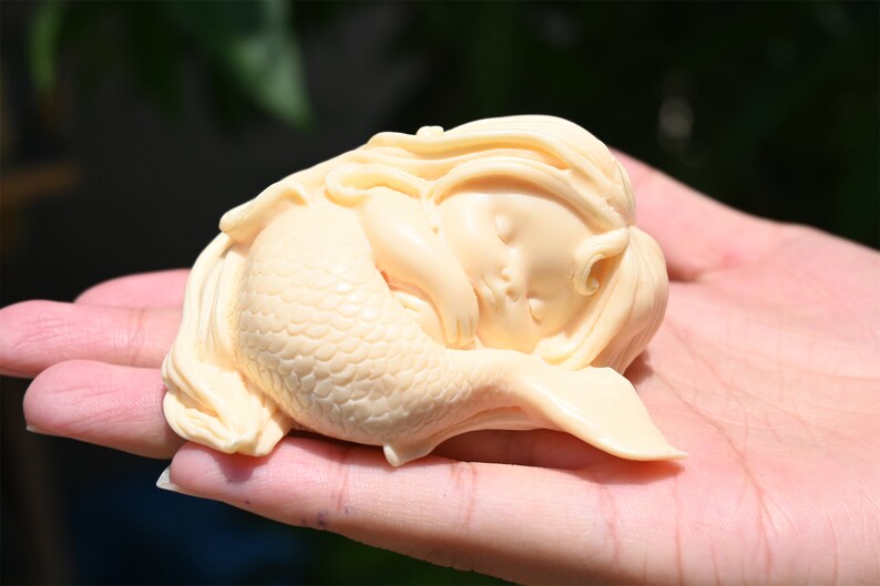 May include: A small, cream-colored sculpture of a sleeping mermaid with a detailed tail and flowing hair.