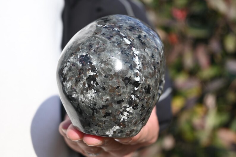 May include: A black and silver skull made of polished stone. The skull has a speckled pattern and a smooth, shiny surface.
