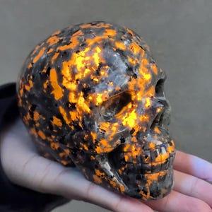 May include: A black and orange skull made of polished stone. The skull has a detailed carving of the facial features and is illuminated from within, creating a glowing effect.