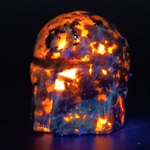 May include: A dark blue and orange helmet made of crystal with a textured surface. The helmet is illuminated from within, creating a glowing effect.