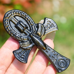 Op de afbeelding: Zwarte en gouden Ankh-hanger met ingewikkelde details. De hanger is gemaakt van een glad, gepolijst materiaal en heeft een glanzende afwerking.