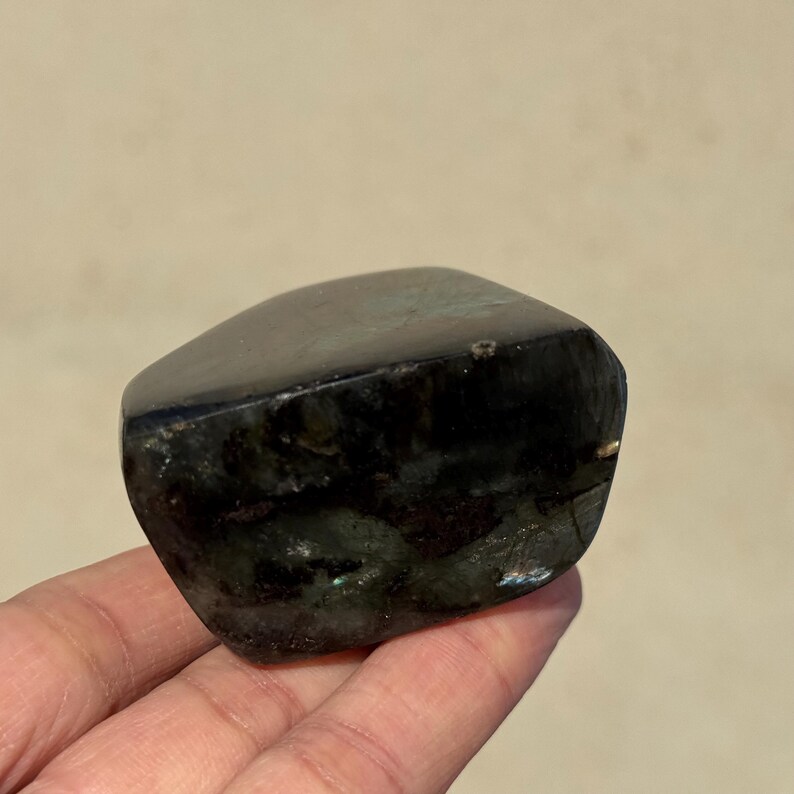 May include: A dark green and black gemstone with a rough, irregular shape. The stone has a smooth, polished surface and is a natural, unfaceted crystal.