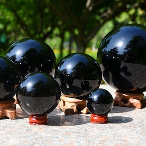 Puede incluir: Un conjunto de seis esferas de obsidiana negra de diferentes tamaños, cada una apoyada en un soporte de madera. Las esferas están altamente pulidas y reflejan la luz, creando un efecto hipnótico.